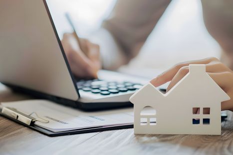 Foto: Person bearbeitet Akten, Modell eines Hauses im Vordergrund